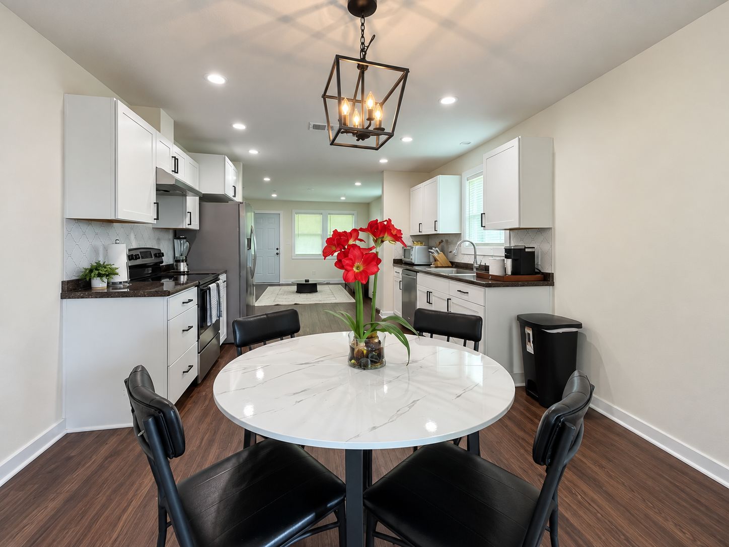 A modern kitchen with white cabinets, a round marble table, and black chairs.