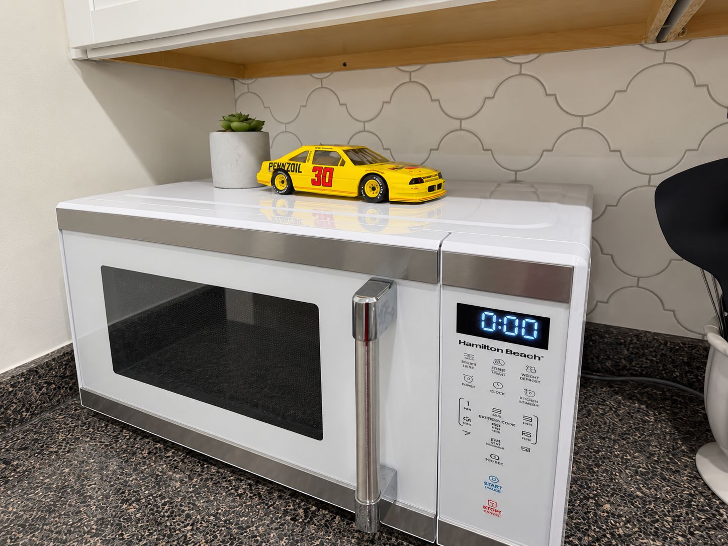 Un four à micro-ondes doté d’un écran numérique, d’un panneau de commande et d’une petite voiture jaune en jouet placée sur le dessus.