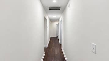 A corridor with white walls, a wooden floor, and a ceiling with recessed lighting and a vent.