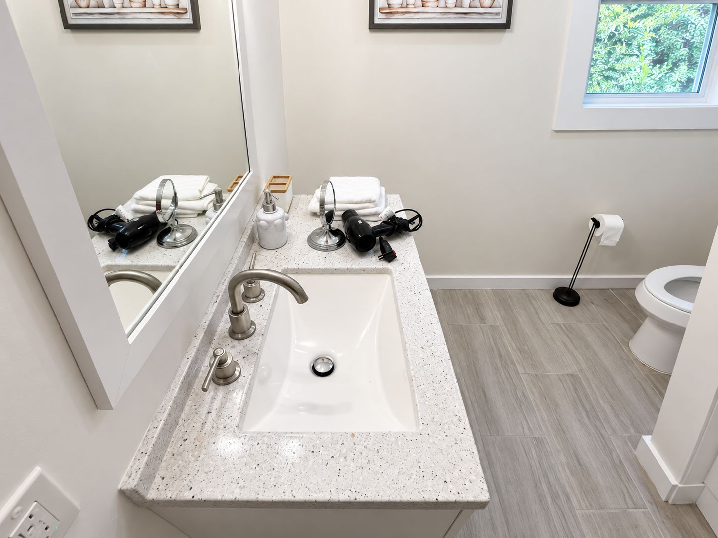 A modern bathroom with a white sink, two faucets, a mirror, and a toilet.