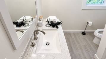 A modern bathroom with a white sink, two faucets, a mirror, and a toilet.