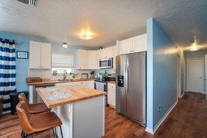 A modern kitchen with white cabinets, a stainless steel refrigerator, and a wooden island with two stools. - Escape to Eden | Sunset Views & Dockage (Big Pine Key)