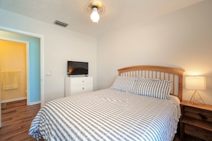 A bedroom with a bed, a television on a stand, a bedside lamp, and a door leading to another room. - Escape to Eden | Sunset Views & Dockage (Big Pine Key)