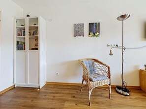 A room with a white cabinet, a wicker chair, a floor lamp, and two wall-mounted artworks. - Edelweiss by Interhome (Farchant)