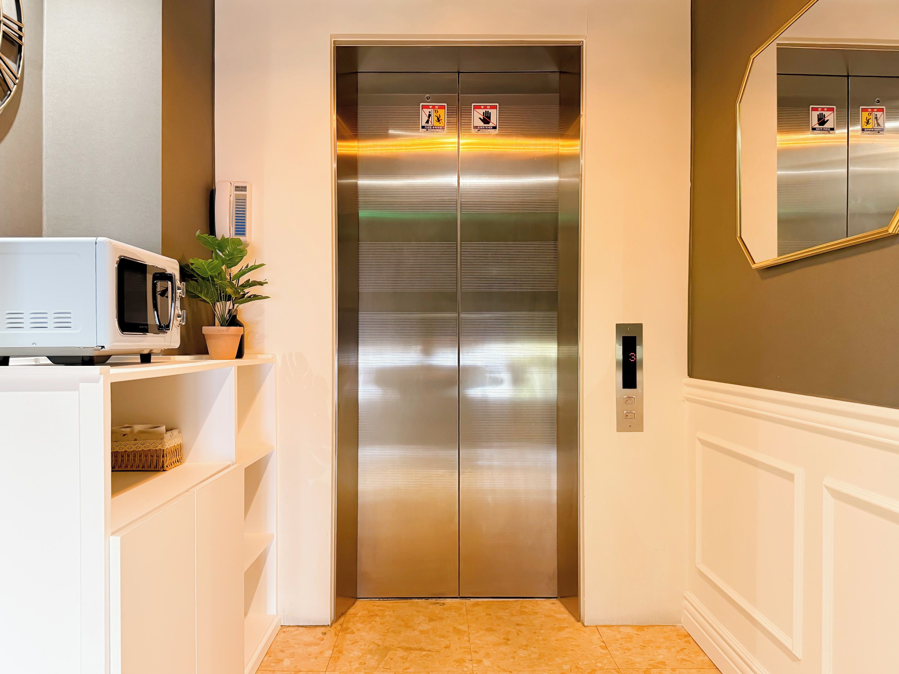 A modern elevator with a digital display, a microwave on a shelf, and a potted plant.