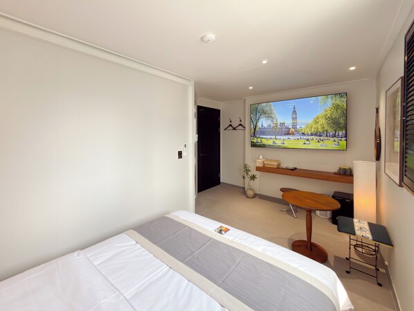 A modern hotel room with a bed, a TV mounted on the wall, a small table, and a bench.