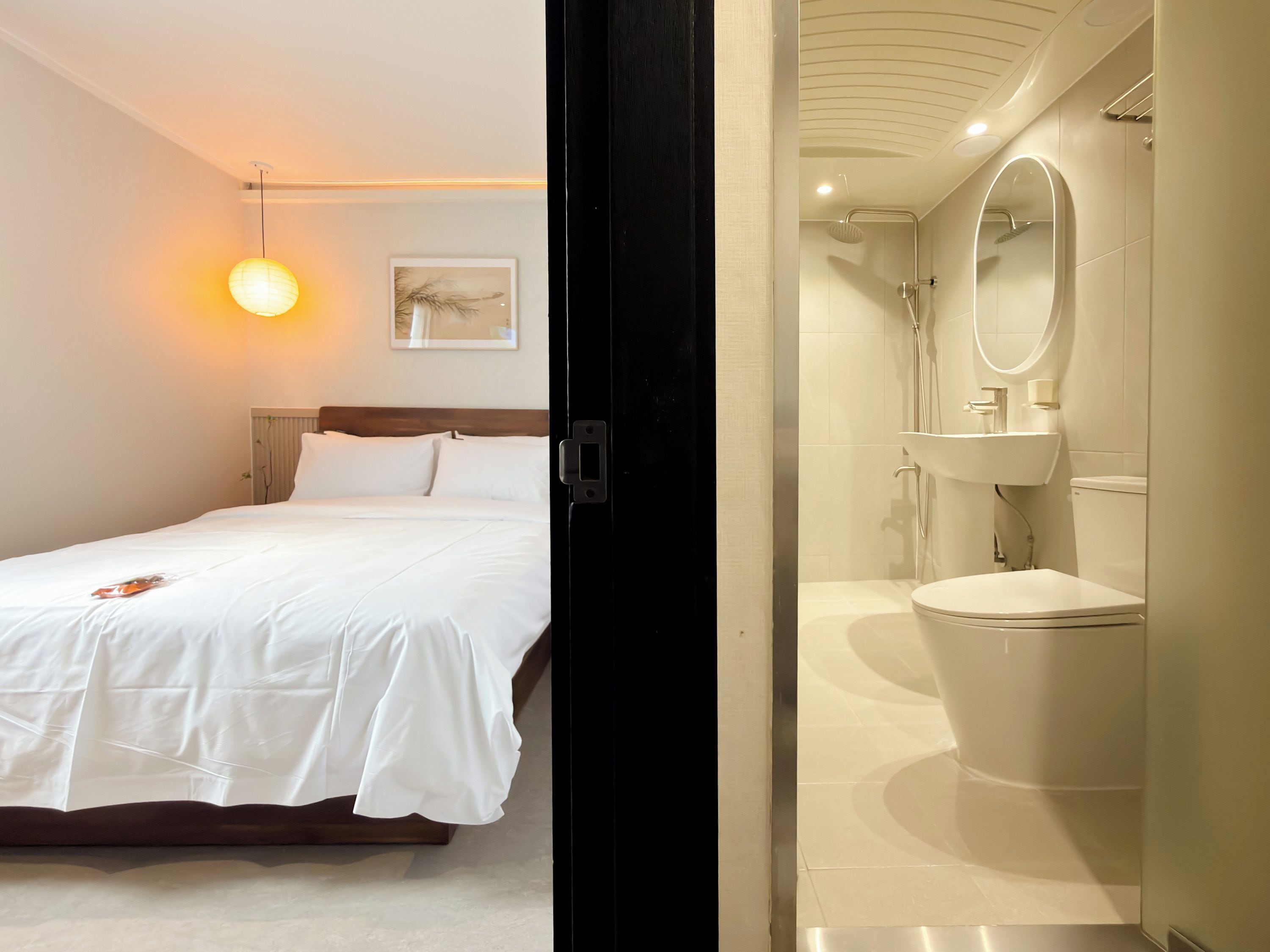 A hotel room with a bed, bedside table, and a wall-mounted lamp.