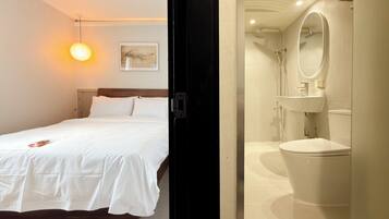 A hotel room with a bed, bedside table, and a wall-mounted lamp.