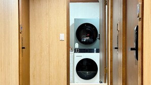 A laundry room with a washing machine and dryer, wooden doors, and a tiled floor. - Unistay (Dongducheon)