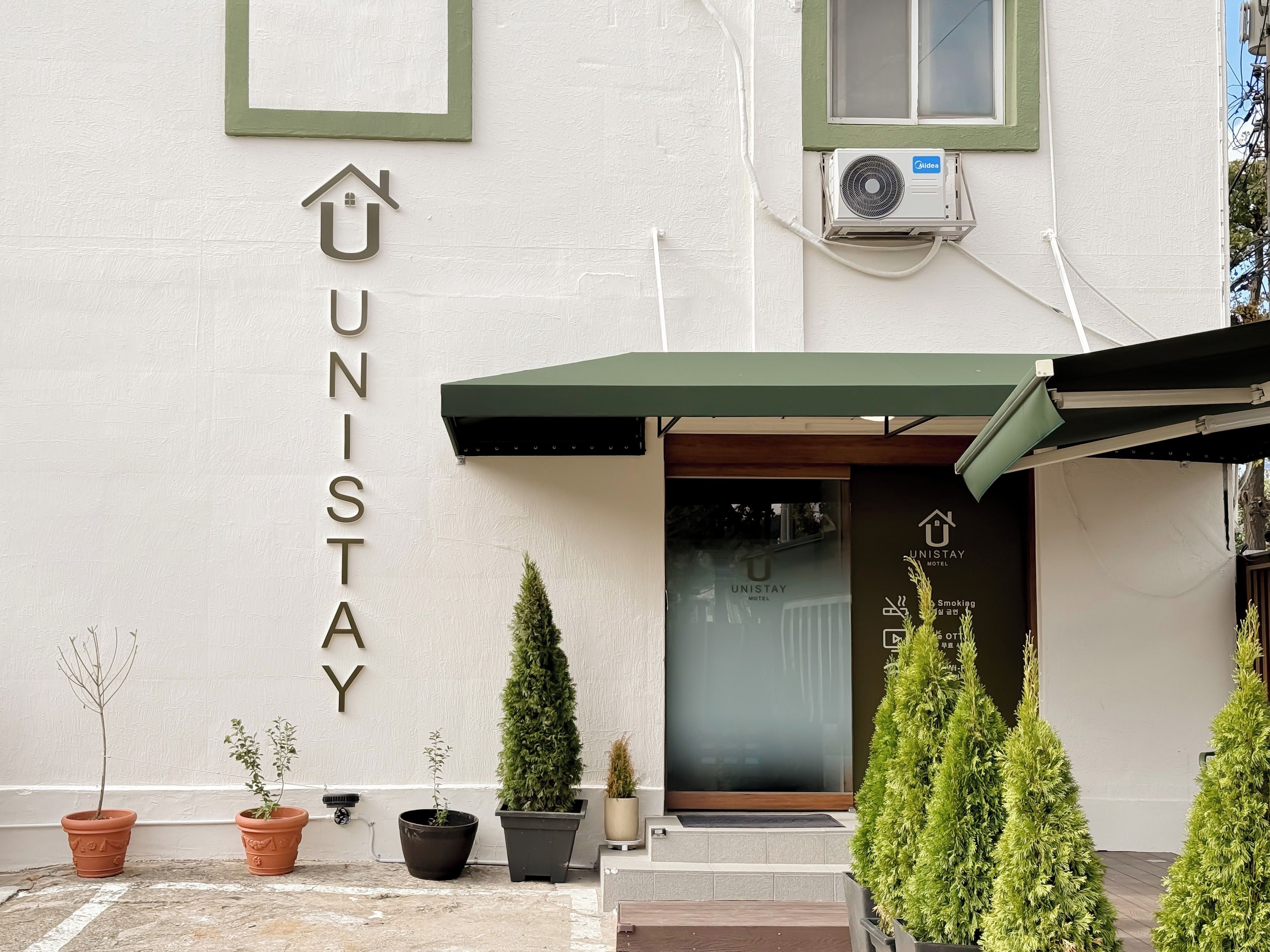 A hotel entrance with a sign reading 'UNISTAY,' a covered entrance, and potted plants.