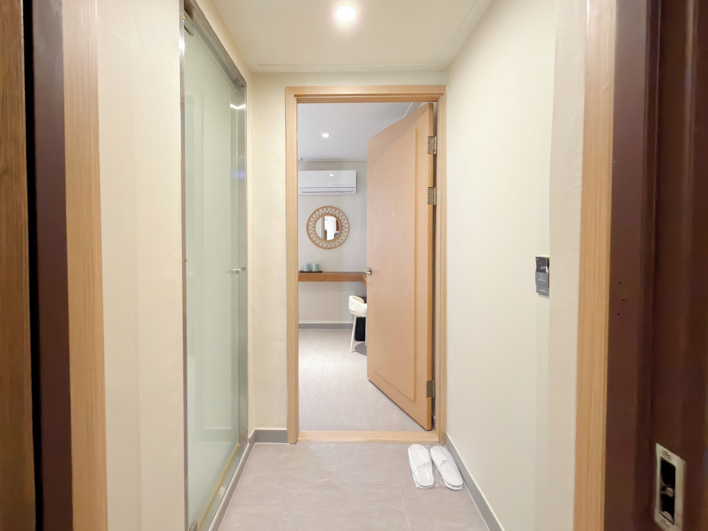 A hallway with a wooden door leading to a bathroom with a mirror and a sink.