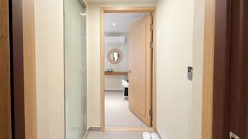 A hallway with a wooden door leading to a bathroom with a mirror and a sink.