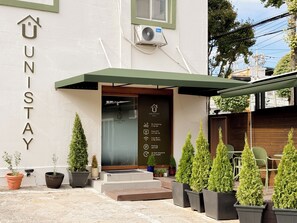 Entrada de un hotel con un cartel que dice 'UNISTAY HOTEL' y servicios indicados como 'No fumar', 'Wi-Fi gratuito' y 'Registro automático 24 horas'.