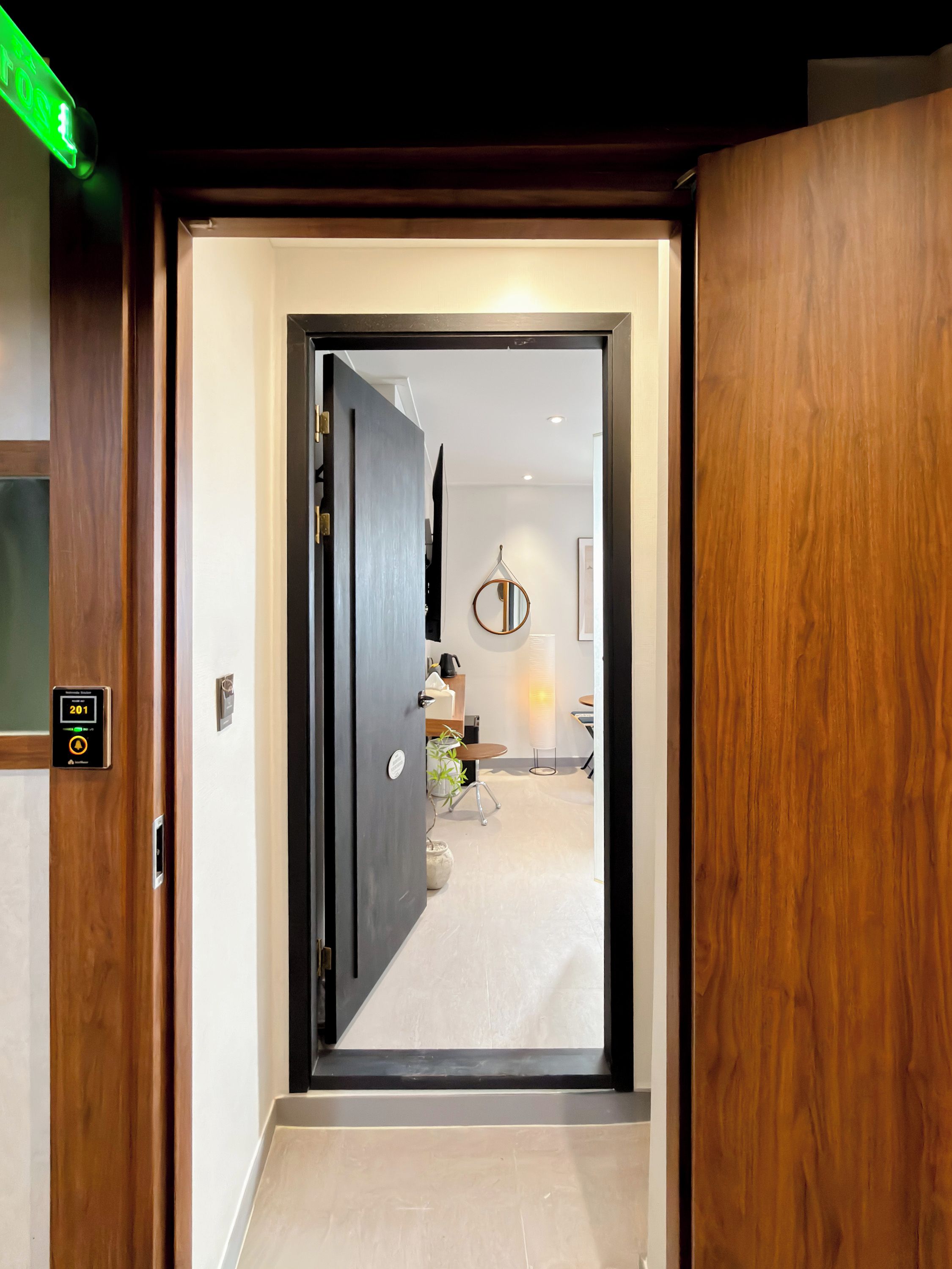 A modern hotel entrance with a digital lock, a wooden door, and a view into a well-lit room with a dining area.