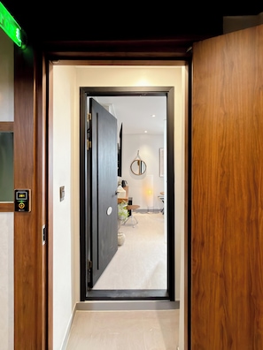 A modern hotel entrance with a digital lock, a wooden door, and a view into a well-lit room with a dining area.