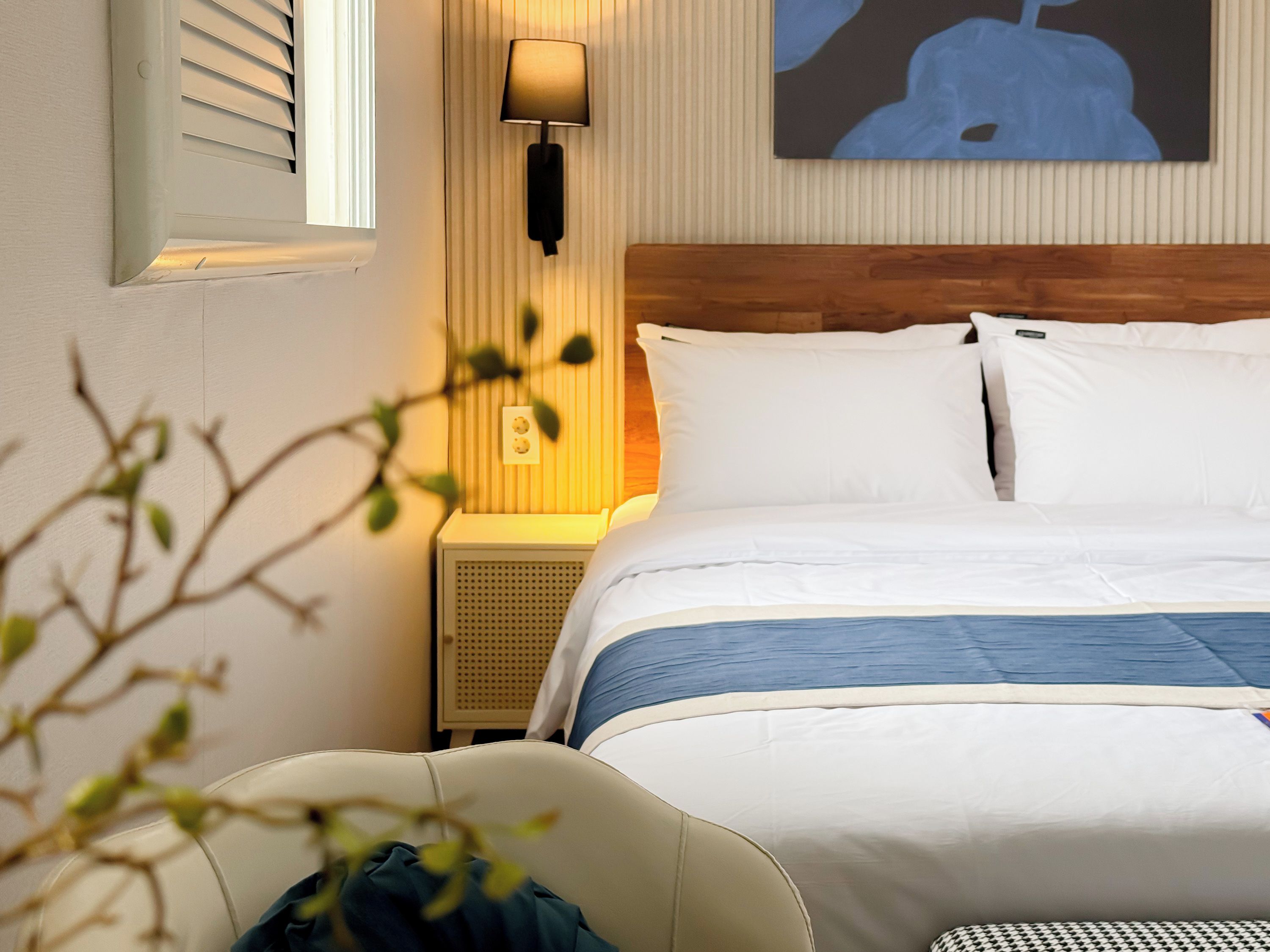 A hotel room with a bed, a bedside lamp, a wall-mounted air conditioner, and a painting.