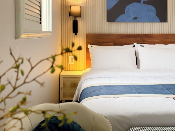 A hotel room with a bed, a bedside lamp, a wall-mounted air conditioner, and a painting.