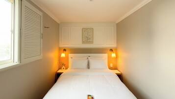 Habitación de hotel con una cama individual, dos lámparas de noche, una ventana con persianas y un cuadro en la pared.