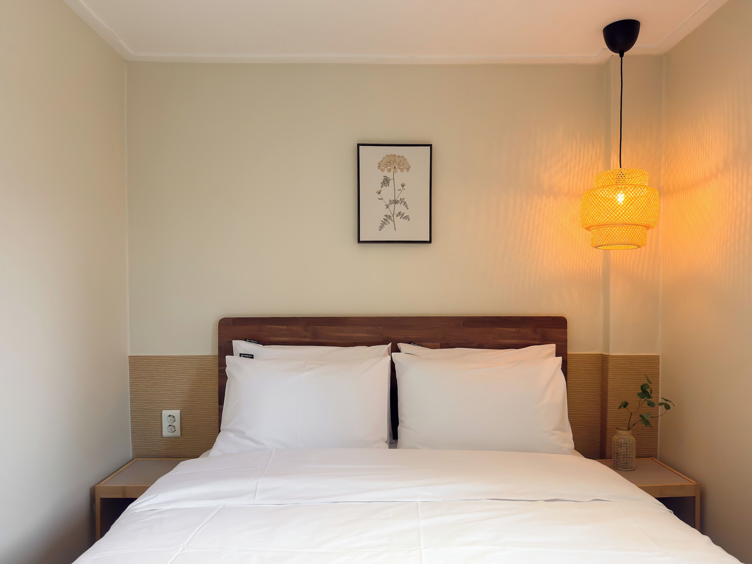 A neatly made bed with white linens, a wooden headboard, and a wall-mounted picture.