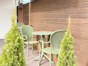 A patio with two green chairs and a table, surrounded by wooden panel walls and small green plants. - Unistay (Dongducheon)