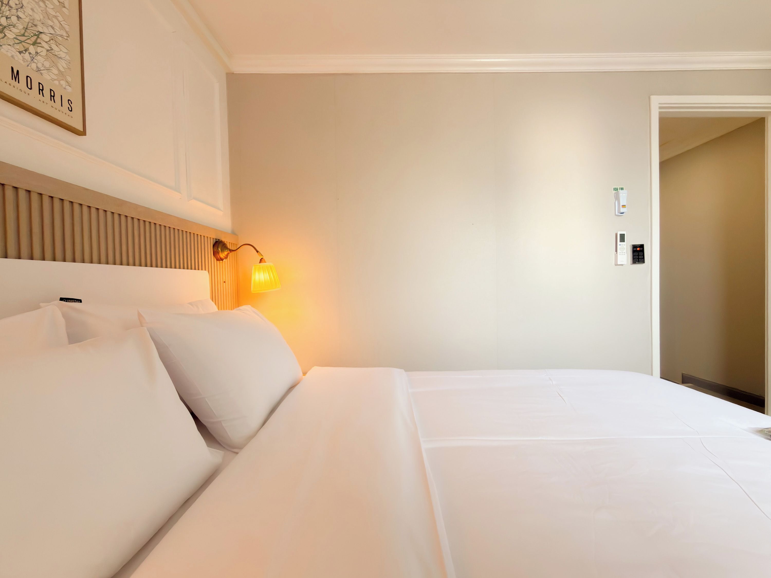 Quarto de hotel com cama, luminária na parede e uma porta.