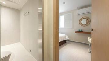A modern bathroom with a shower, toilet, and a visible bed in the adjacent room.