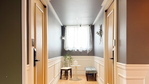 A hallway with a white bench, a small table, and a window with a white curtain. - Unistay (Dongducheon)