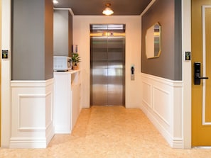 A hallway with a marble floor, a coffee machine, a potted plant, and an elevator.