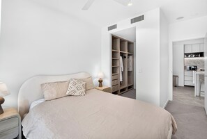 A bedroom with a bed, bedside table, lamp, and a walk-in closet. - Million Dollar Views - Luxe 62nd Floor Apartment (Brisbane City)