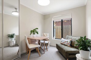 A modern living room with a dining area, a sofa, and a large window with a view. - Broadleaf by the Beach | Glenelg South (Glenelg South)