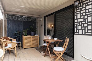 Een terras buiten met rieten meubels, een houten tafel en potplanten.