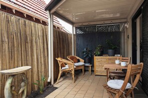 A patio area with wicker furniture, a table, chairs, and a decorative fence. - Broadleaf by the Beach | Glenelg South (Glenelg South)