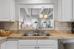A kitchen with a double sink, a stainless steel faucet, a marble countertop, and a built-in dishwasher. - Golf Course Retreat in Queens Grant: Private Deck, Pool Access, Near Shelter Cove (Hilton Head Island)