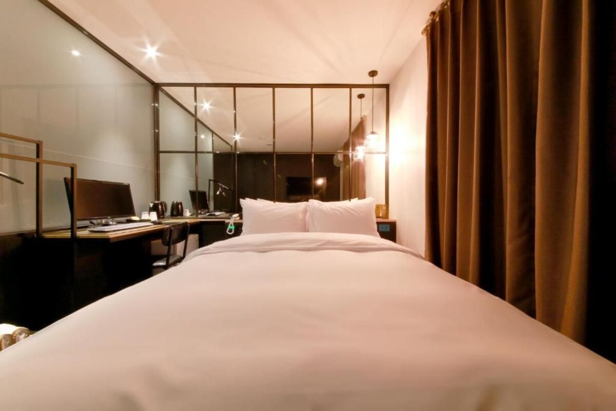 Quarto de hotel com uma cama grande, uma escrivaninha com computador, uma cadeira e um espelho.