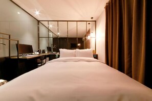 Quarto de hotel com uma cama grande, uma escrivaninha com computador, uma cadeira e um espelho.