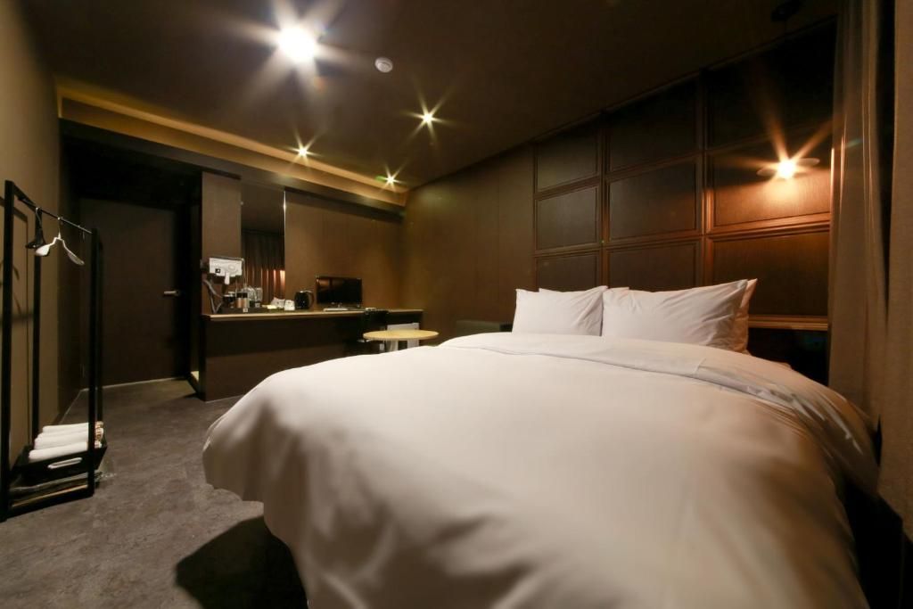 A hotel room with a large bed, a desk with a chair, a mirror, and a wardrobe.