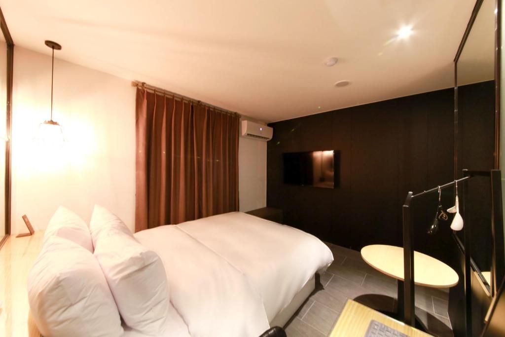 A hotel room with a bed, a bedside table, a desk, a chair, a mirror, and a window with curtains.