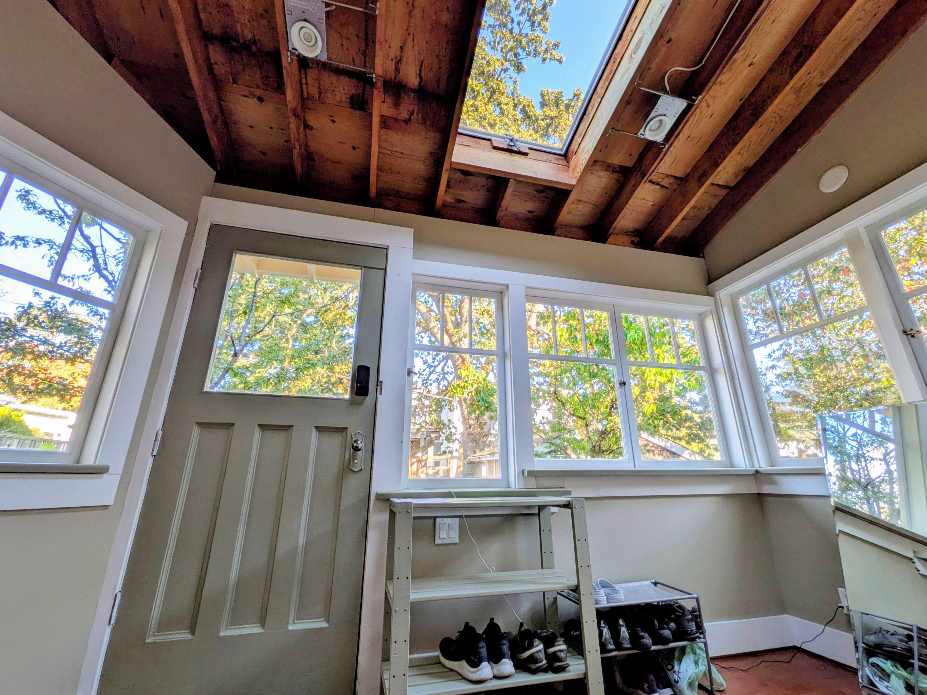 Una habitación con techo de madera, ventanas amplias, una puerta y un zapatero.