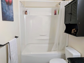 Une salle de bain avec une baignoire, des toilettes et une étagère contenant des articles de toilette.