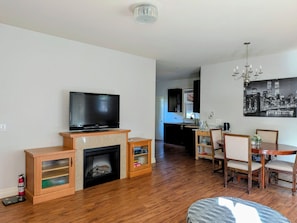 A living room with a fireplace, a television, a dining area with chairs and a table, and a kitchen in the background.