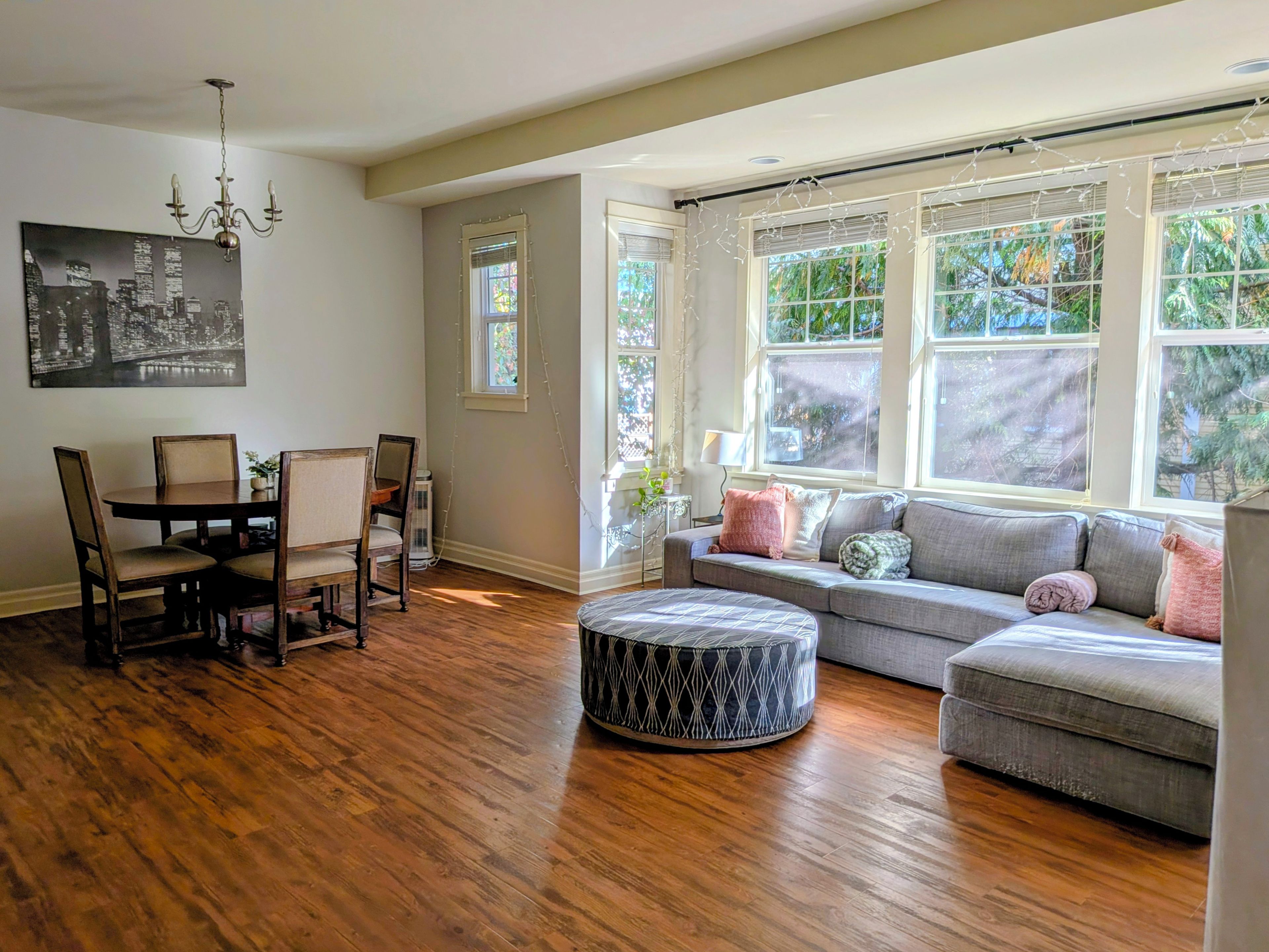 A dining area with a wooden table and chairs, a gray sofa, and a patterned ottoman.