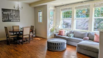 A dining area with a wooden table and chairs, a gray sofa, and a patterned ottoman.