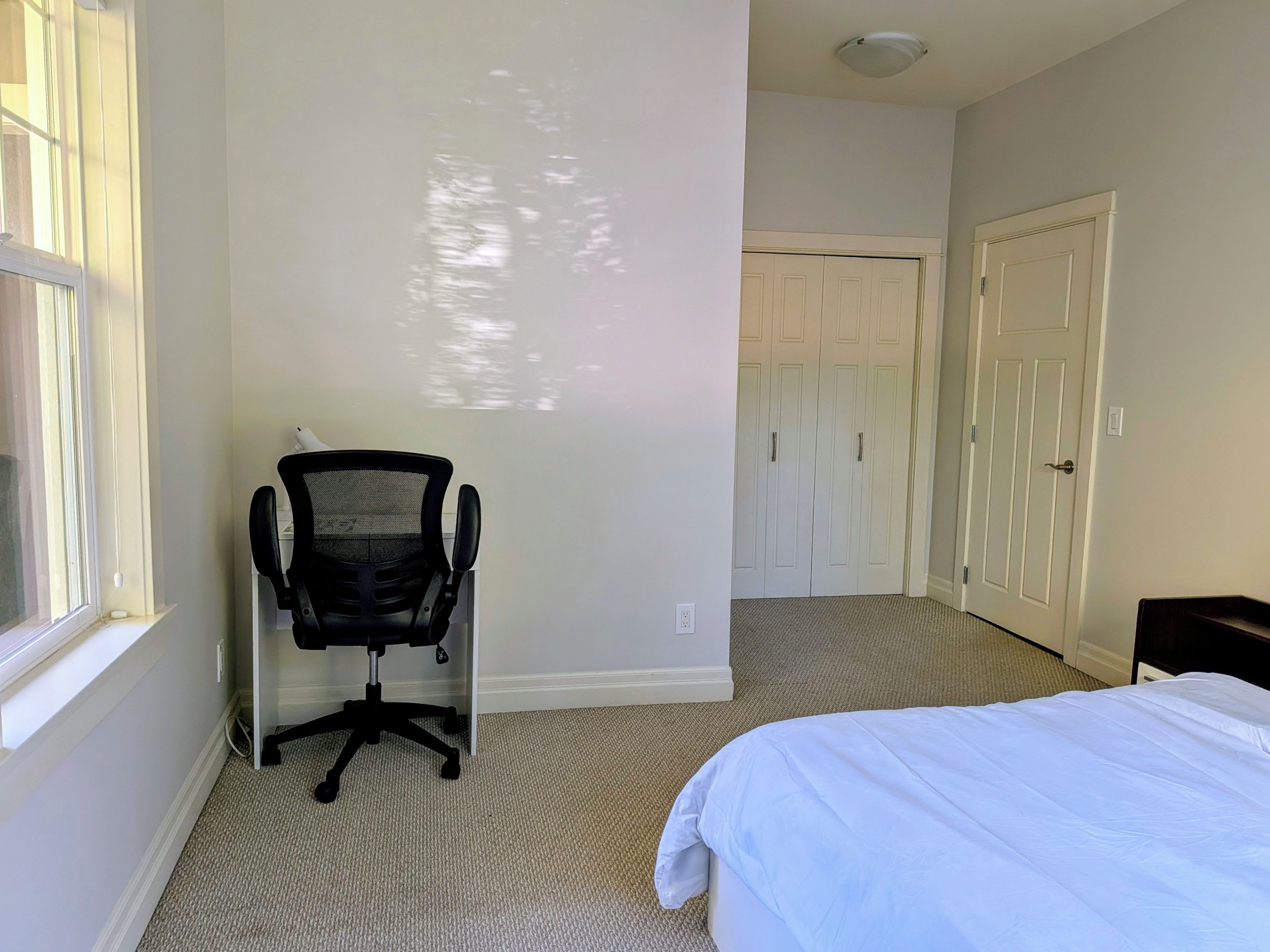 A bedroom with a bed, a chair, a closet, and a window.
