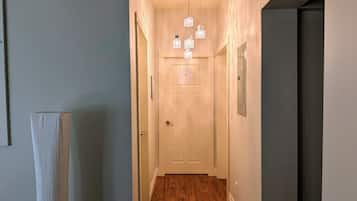 A hallway with a wooden floor, a white door, and a hanging light fixture.