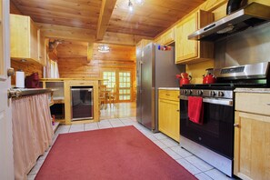 A kitchen with wooden cabinets, a stainless steel refrigerator, a stove, and a red rug. - Private House with access to Stinson Lake! Enjoy lake life in style! (Rumney)