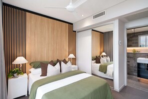 Ein modernes Schlafzimmer mit einem großen Bett, zwei Nachttischen mit Lampen, einem Spiegel und Blick auf ein Badezimmer.