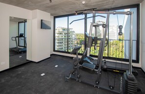 Uma academia com equipamentos de ginástica, esteira e uma grande janela com vista para a cidade.