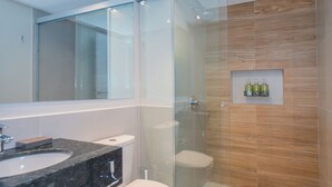 Un baño moderno con ducha de vidrio, inodoro blanco y lavamanos de mármol.