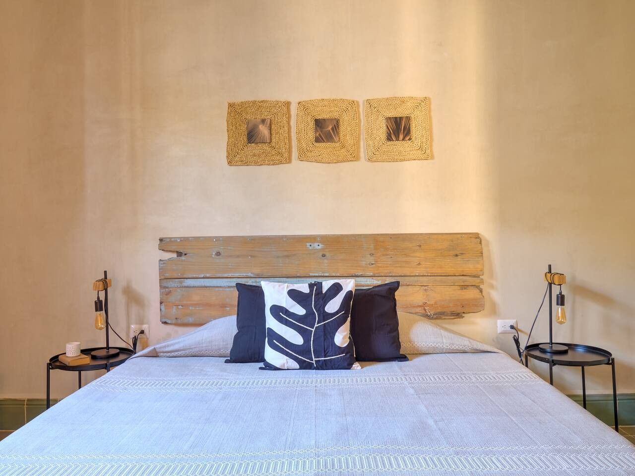 Un letto rifatto con cura, con una testiera in legno, due comodini con lampade e tre quadri appesi al muro.
