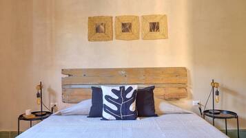 Un letto rifatto con cura, con una testiera in legno, due comodini con lampade e tre quadri appesi al muro.